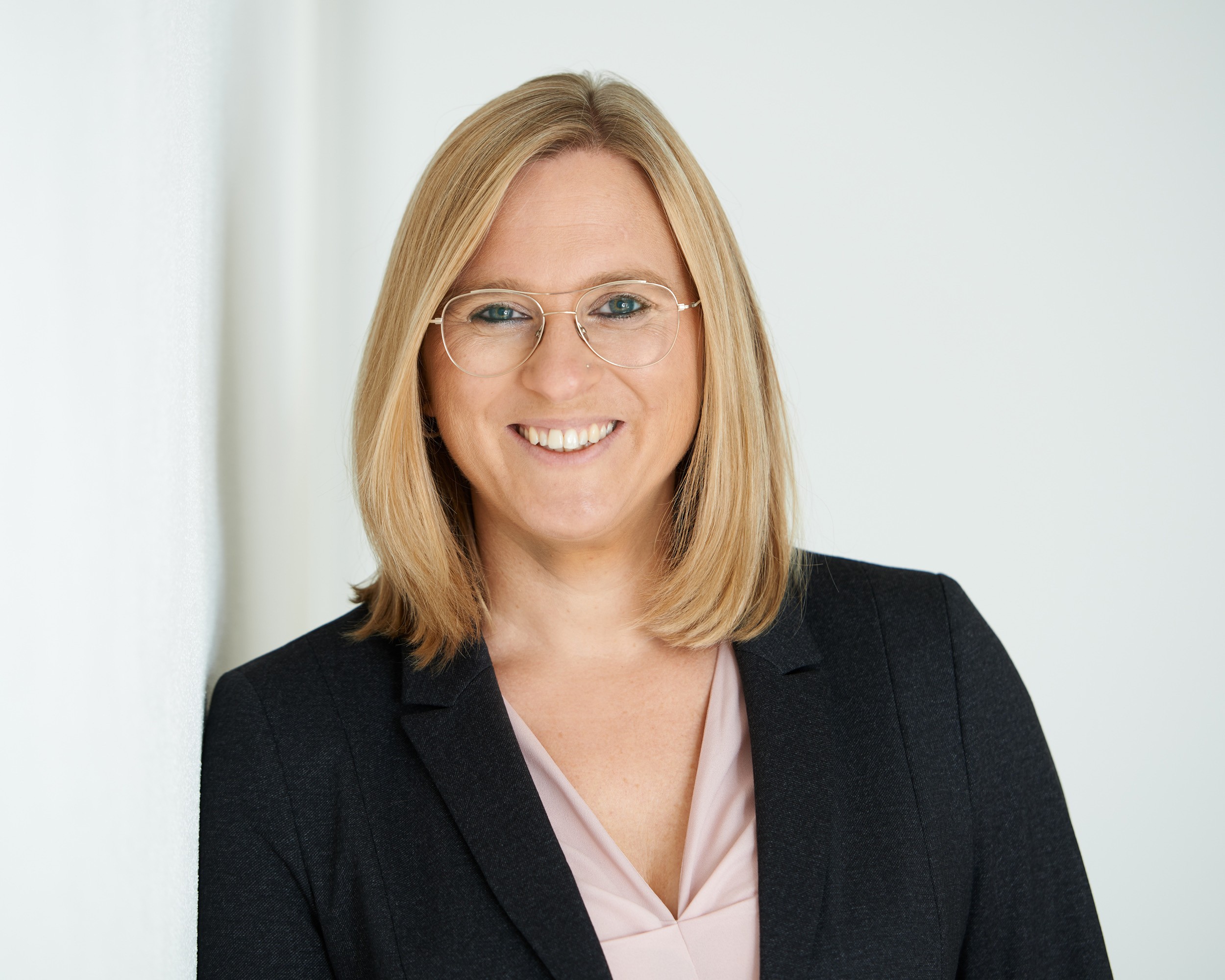 Das Bild zeigt die Geschäftsführerin Yvonne Schnellbacher, die vor einem neutralen, hellen Hintergrund steht. Sie trägt ein dunkelgraues Sakko, darunter ist eine hellrosa Bluse mit einem V-Ausschnitt sichtbar. Yvonne Schnellbacher hat schulterlanges, blondes Haar. Der Hintergrund ist schlicht und in einem hellen Weißton gehalten, wodurch der Fokus auf die Person gelenkt wird. Das Bild vermittelt einen freundlichen, professionellen und seriösen Eindruck. Das Bild zeigt die Geschäftsführerin Yvonne Schnellbacher, die vor einem neutralen, hellen Hintergrund steht. Sie trägt ein dunkelgraues Sakko, darunter ist eine hellrosa Bluse mit einem V-Ausschnitt sichtbar. Yvonne Schnellbacher hat schulterlanges, blondes Haar. Der Hintergrund ist schlicht und in einem hellen Weißton gehalten, wodurch der Fokus auf die Person gelenkt wird. Das Bild vermittelt einen freundlichen, professionellen und seriösen Eindruck.
